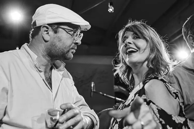 Singer and fellow musician sharing a smile beneath the stage lights, in black and white — Jazz photography by Michaël Gramm