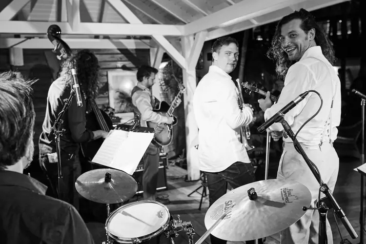 Jazz musicians sharing a smile, seen from behind the drum kit in black and white — Jazz photography by Michaël Gramm